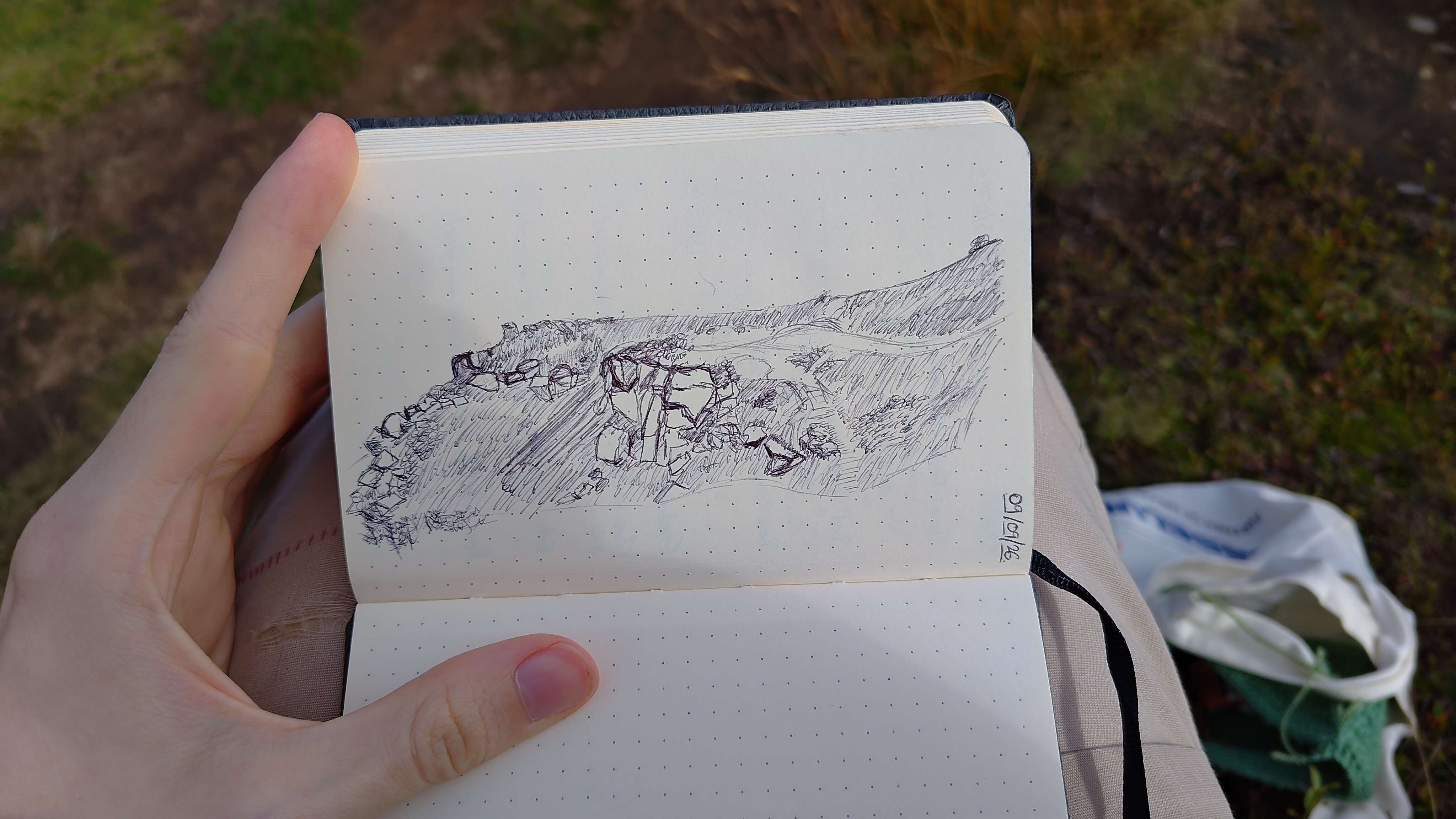 A photo of a notebook with a sketch in pen of a landscape. There are cliffs and rocks scattered over the landscape.