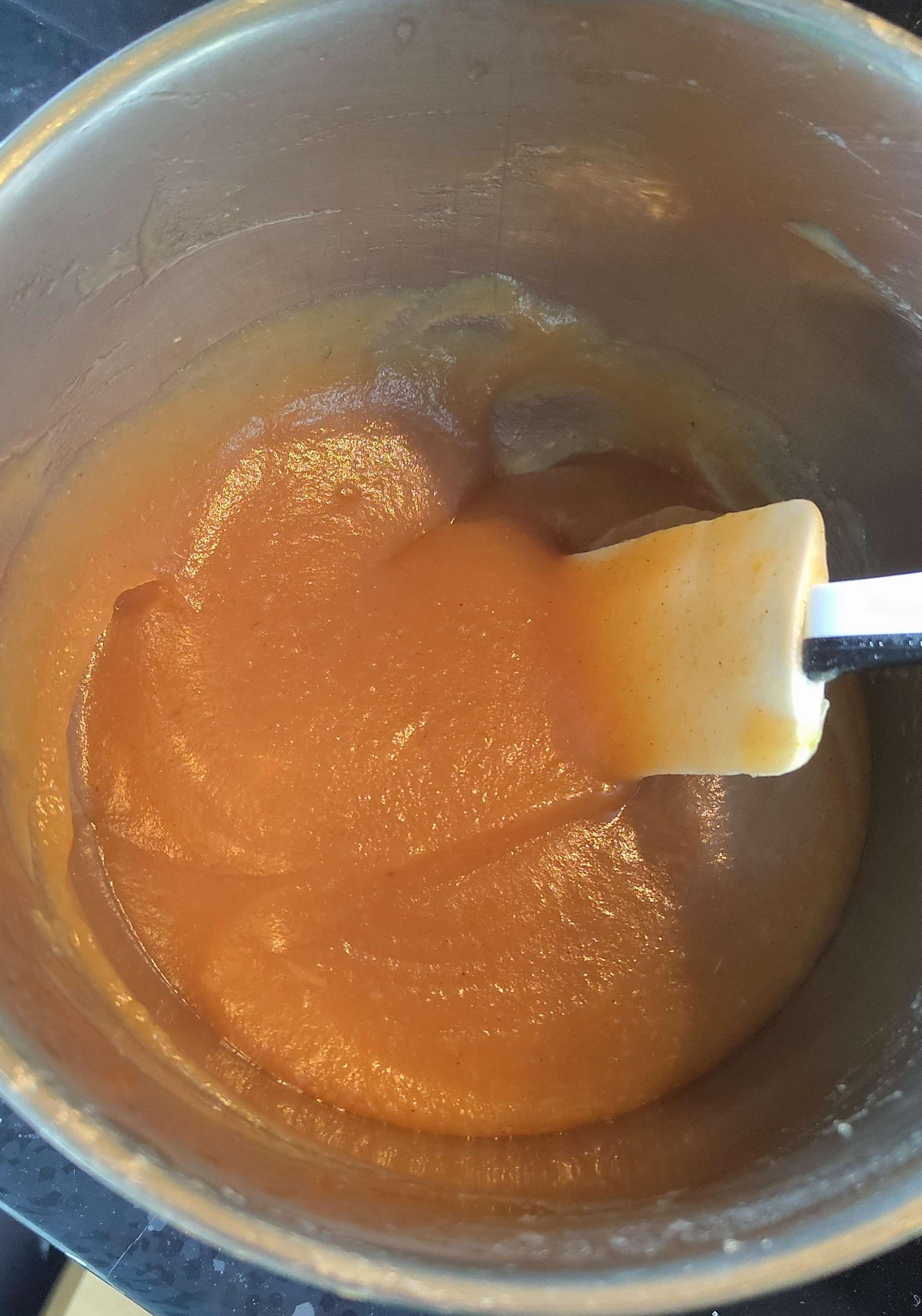 A photo of a pan with a white spatula in it. Inside is a light brown liquid, of apple pulp and juice.